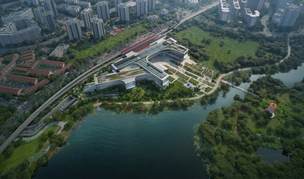 Aerial view of a modern building complex next to a lake and parkland, with city buildings in the background.